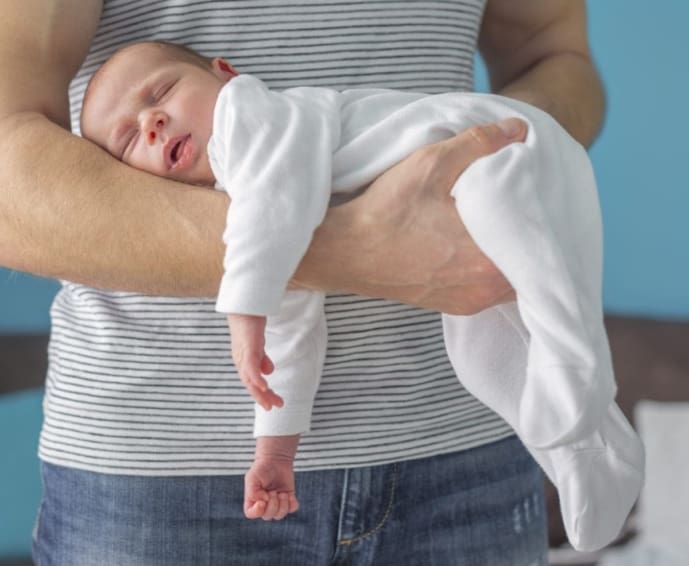 Baby sleeping in a position on his father’s arm to help treat colic