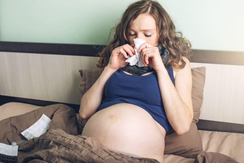 Young pregnant woman in bed with pills and a thermometer. Sick with the flu or a cold.