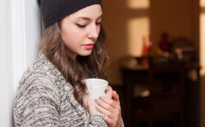 Sad-looking young woman with dysthymic disorder, or PDD, looks down while holding a mug.