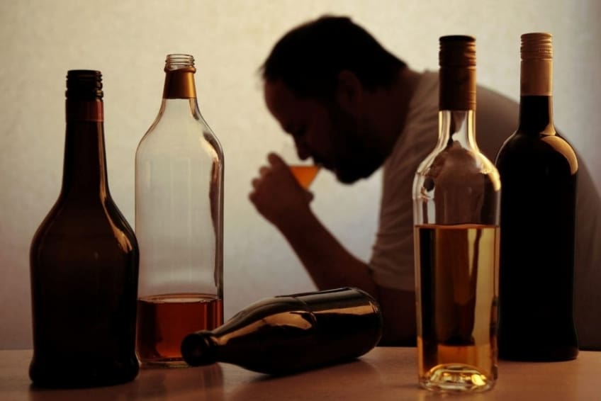 silhouette of a person drinking, sitting behind bottles of alcohol