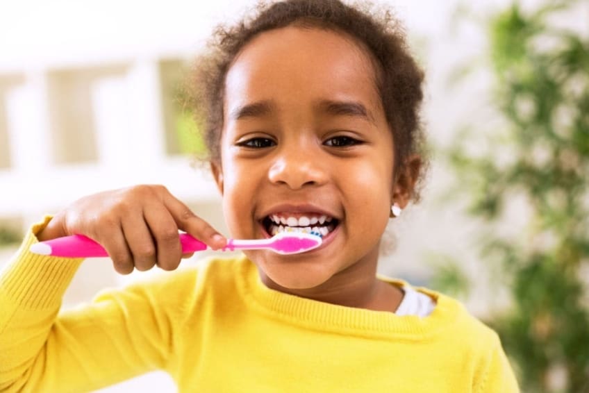 Little girl brushing her teeth and smiling