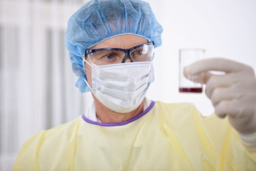 A doctor wearing protective gear while handling a blood sample