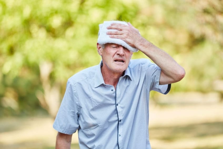 Senior man with heat exhaustion cools his head with a wet cold cloth
