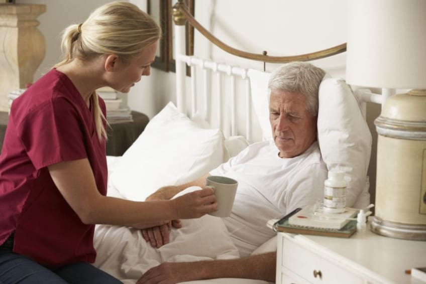 Nurse providing care to elderly man at home in bed
