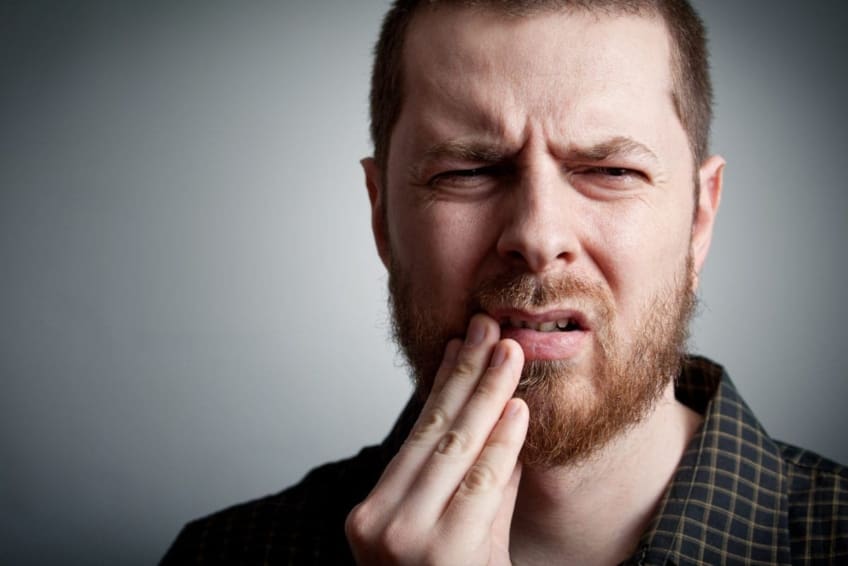 A man holds his mouth in pain. Burning mouth syndrome (BMS) is marked by pain and discomfort in the mouth, lips, and/or tongue.