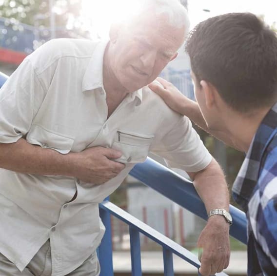 An older man bent over in pain holding his chest