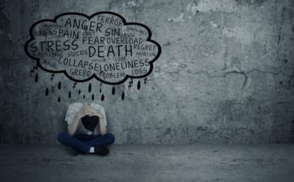 Depressed teenage boy sitting alone with word cloud describing symptoms of depression