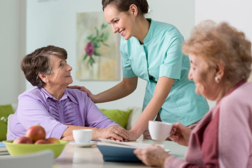 Two older women visiting with nurse in nursing home