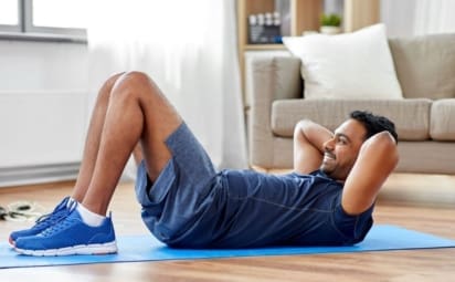 A man does sit ups on a mat on the floor as part of his exercise routine.