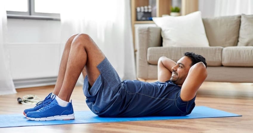 A man does sit ups on a mat on the floor as part of his exercise routine.