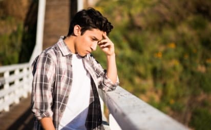Sad-looking teenage boy standing on a bridge thinking about suicide