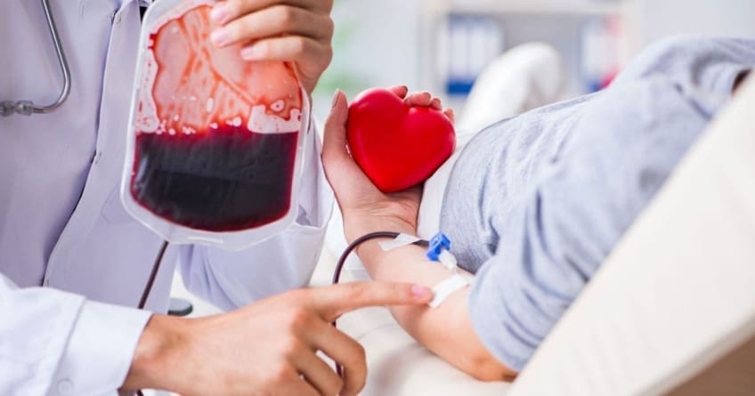 A doctor holds a bag of blood while talking to patient getting a blood transfusion because of anemia symptoms.