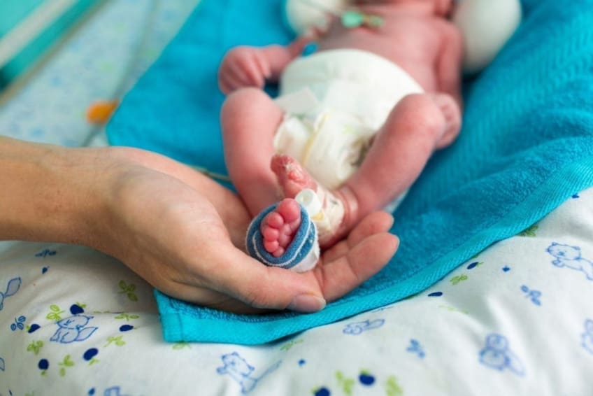 Mother holding premature baby’s feet with neonatal infant pulse oximeter