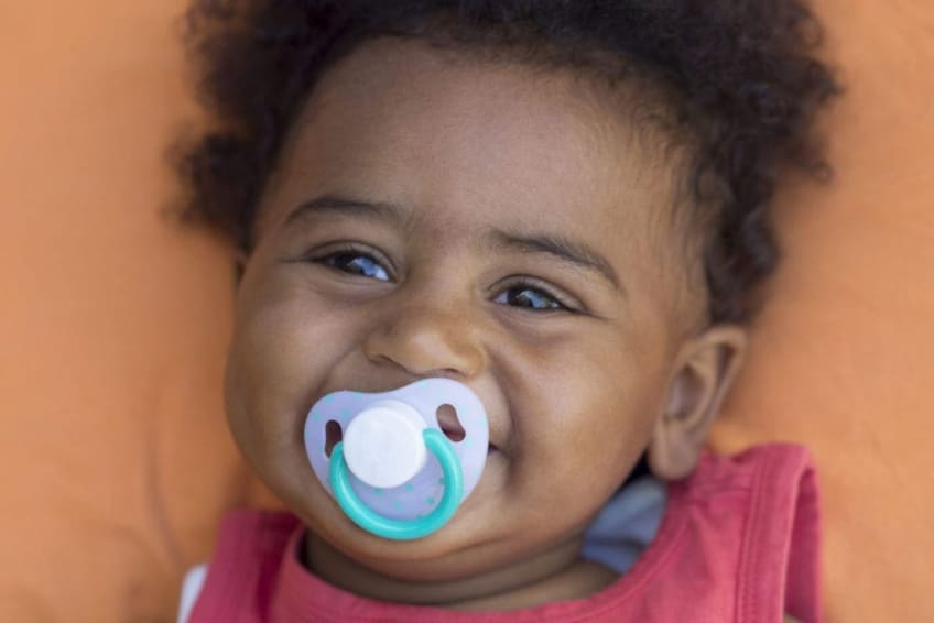baby boy smiles as he sucks on a pacifier