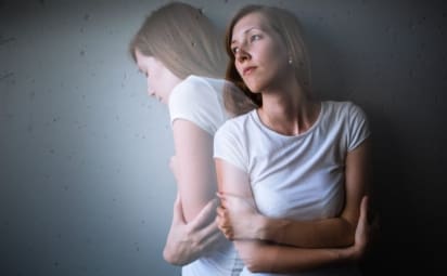 Young woman suffering from depression/anxiety stands with her arms crossed.
