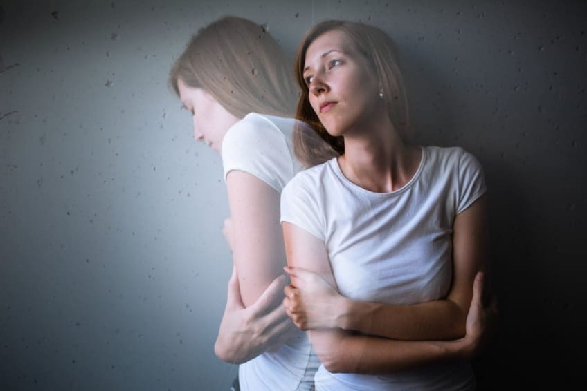 Young woman suffering from depression/anxiety stands with her arms crossed.