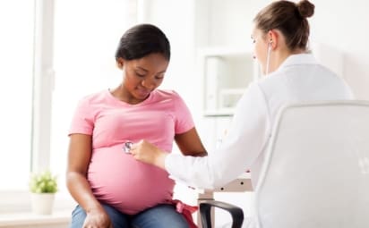 doctor listens to a pregnant woman’s belly with a stethoscope