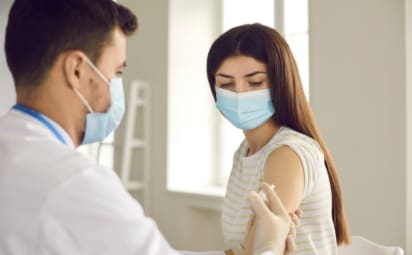 Doctor giving vaccine shot to young woman during immunization campaign at clinic
