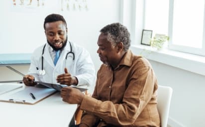 A doctor wearing a white coat sits with a patient in his office to go over the benefits of the RSV vaccine.