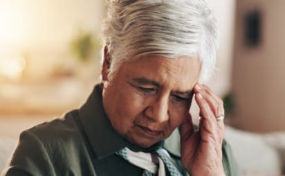 A woman holds her hand to her forehead as if she is struggling to recall something.